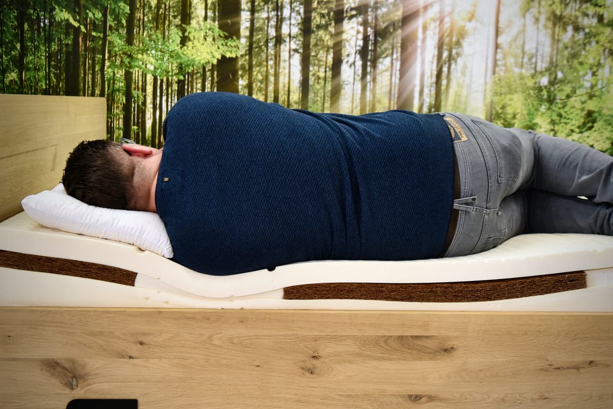 Kunde liegt auf Matratze im Holzbett – Gesamtsystem aus Bettrahmen, Lattenrost und Matratze